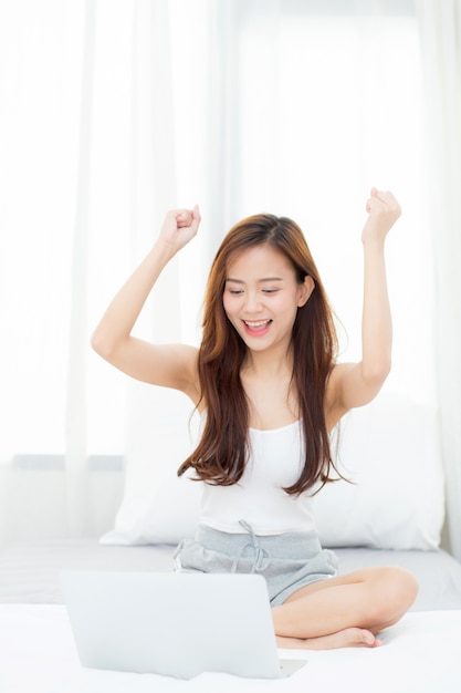 La mujer asiática de la felicidad hermosa que usa la computadora portátil trabaja con éxito.