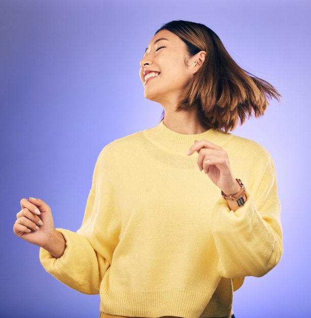 Mujer asiática feliz bailando y música en libertad o moda casual contra un fondo de estudio púrpura Persona femenina o modelo sonriendo disfrutando de un evento de energía o fiesta en felicidad para la ropa en la maqueta