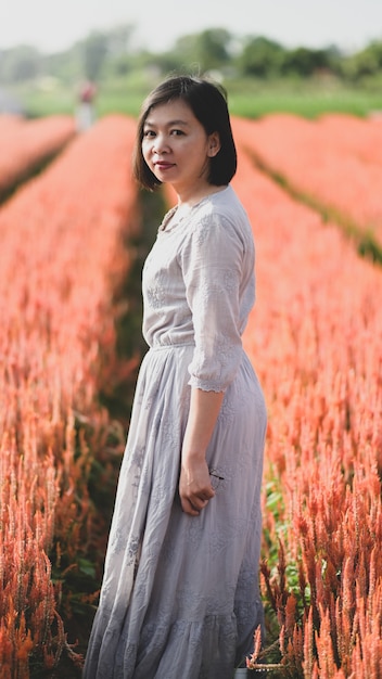 Mujer asiática feliz caminando y tomando fotografías en el jardín de flores, mira a la cámara y sonríe, foto vertical.