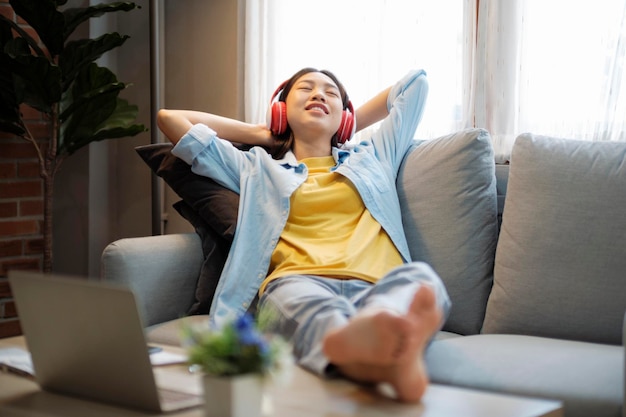 Mujer asiática feliz escuchando música mientras se recuesta en el sofá