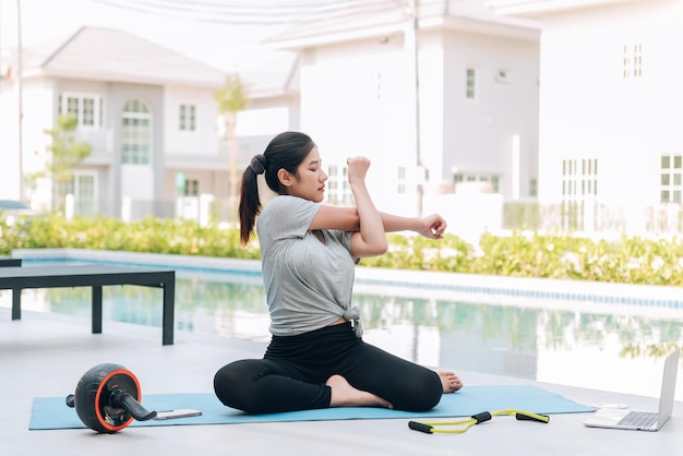 Mujer asiática feliz haciendo ejercicio de estiramiento y entrenamiento de yoga por la mañana en casa al aire libre