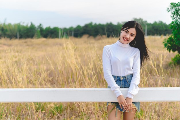 Mujer asiática feliz con hermoso puesto en la valla en el estilo de vida de campo de una chica soltera