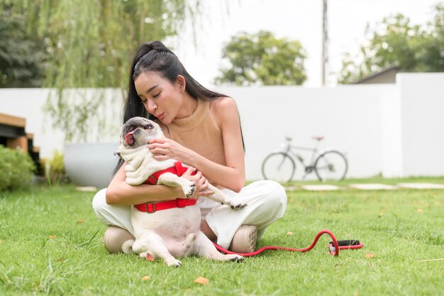 Una mujer asiática feliz jugando con un perro cachorro lindo y inteligente en el patio trasero.