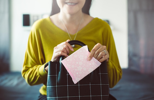 Mujer asiática feliz mano poniendo servilleta sanitaria en el bolso, almohadilla menstrual blanca, menstruación