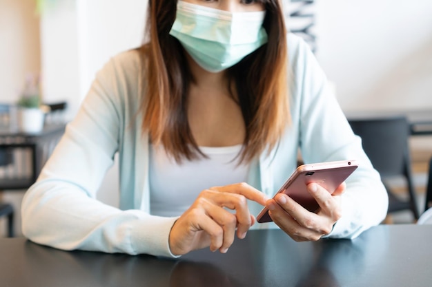 Mujer asiática feliz con máscara médica usando teléfono móvil en café Tecnología y estilo de vida Concepto de atención médica Primer plano