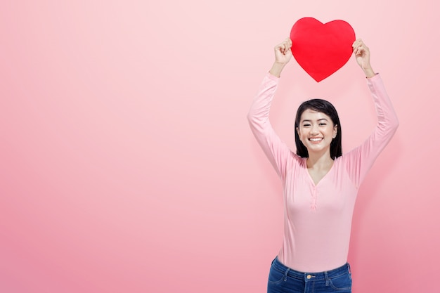 Mujer asiática feliz que lleva a cabo el corazón rojo