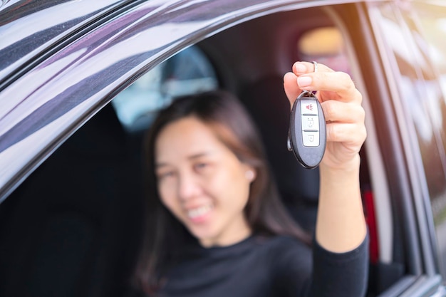 Una mujer asiática feliz que muestra la clave de su nuevo negocio de transporte de automóviles