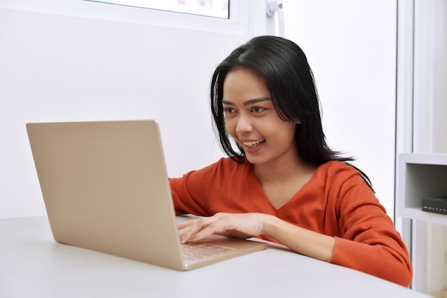 Mujer asiática feliz que usa una computadora portátil mientras que se sienta