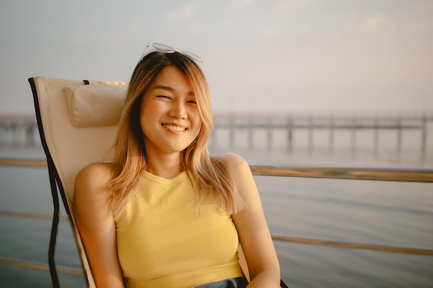 Mujer asiática feliz se sienta y relajada disfruta de la vista del mar al atardecer de su luna de miel