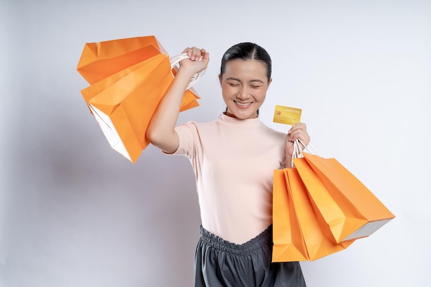 Mujer asiática feliz sonriendo sosteniendo bolsas de compras y tarjeta de crédito aislado sobre fondo blanco.