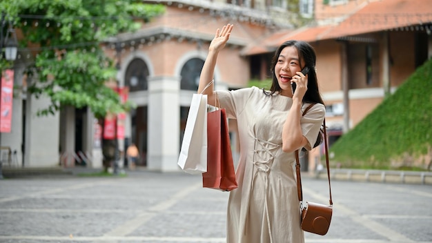 Una mujer asiática feliz con sus bolsas de compras está hablando por teléfono con su amiga en la calle