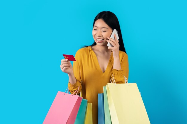 Mujer asiática feliz con tarjeta bancaria telefónica y compras