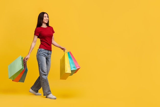 Una mujer asiática feliz con un traje casual caminando con bolsas de compras.