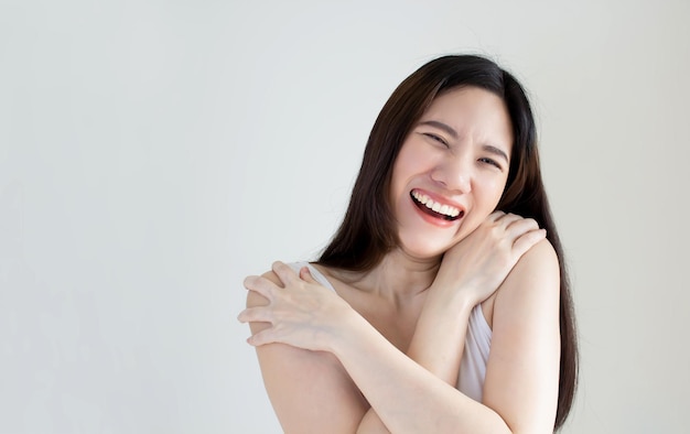 La mujer asiática feliz usa una camiseta blanca que se abraza a sí misma, está sonriendo y riendo con despreocupación. Concepto de vida saludable Buena salud mental.