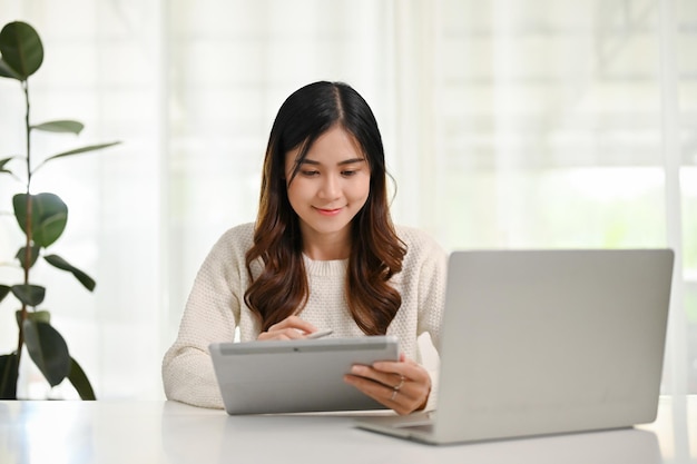 Mujer asiática feliz usando su tableta digital en una mesa en su oficina en casa