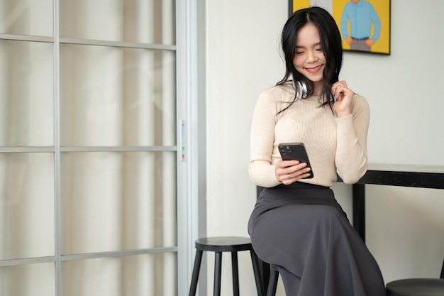 Una mujer asiática feliz usando su teléfono inteligente mientras se relaja en una cafetería