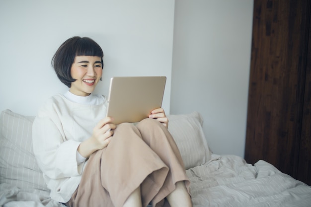 Mujer asiática feliz usando la tablet en el dormitorio.