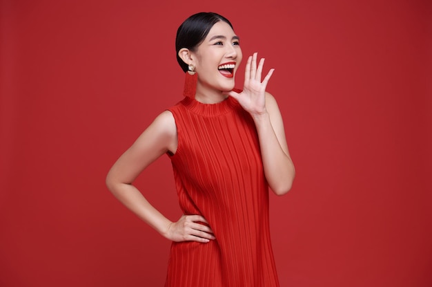 Una mujer asiática feliz con un vestido rojo con la boca abierta levantando las manos gritando un anuncio