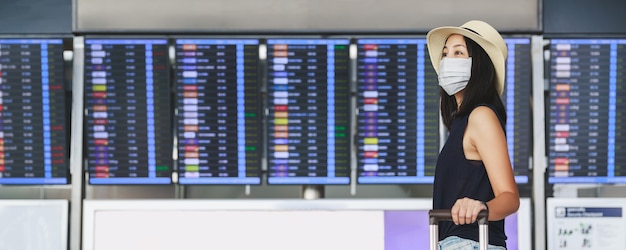 Mujer asiática feliz viajero con máscara y equipaje distanciamiento social y caminar en la terminal del aeropuerto