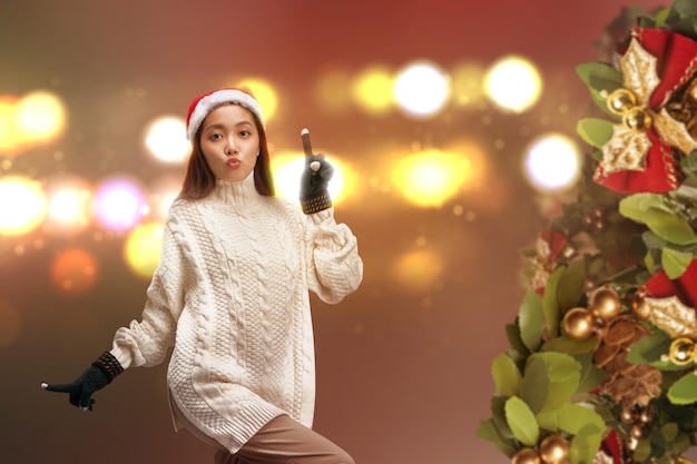 Mujer asiática con guantes de invierno y gorro de Papá Noel de pie con fondo claro borroso