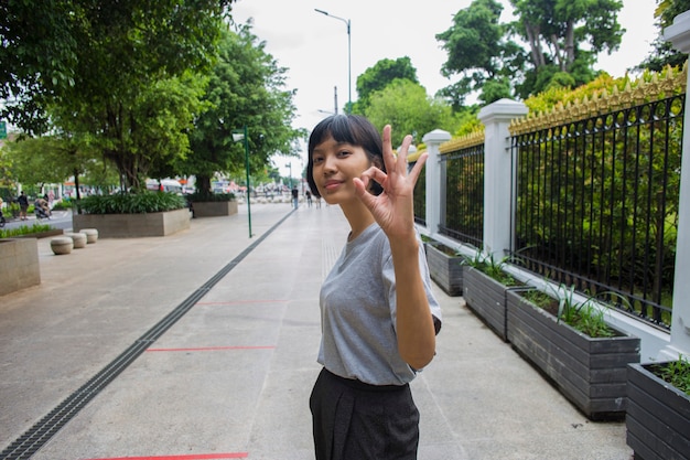 Mujer asiática hace gesto de pulgar hacia arriba en espacios públicos