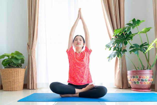 Mujer asiática haciendo ejercicio en su sala de estar con colchoneta de yoga en casa