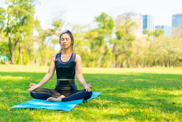 Mujer asiática haciendo ejercicio de yoga y relajarse con ropa deportiva en el parque verde en verano