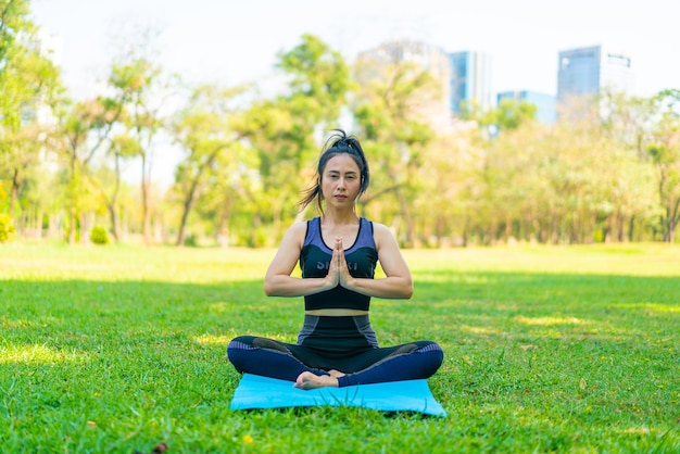 Mujer asiática haciendo ejercicio de yoga y relajarse con ropa deportiva en el parque verde en verano