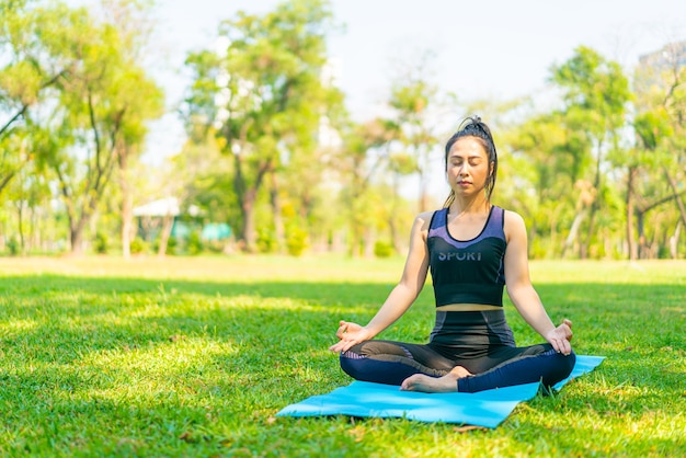 Mujer asiática haciendo ejercicio de yoga y relajarse con ropa deportiva en el parque verde en verano