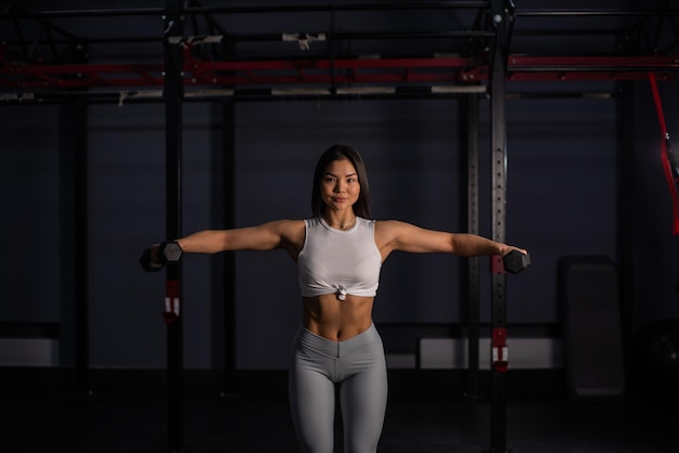 Mujer asiática haciendo ejercicios con pesas en el gimnasio.