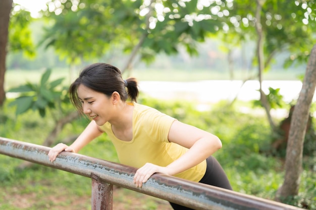 Foto mujer asiática haciendo flexiones con empuñaduras de hierro en el parque