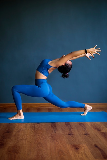 Mujer asiática haciendo pose de yoga en estera azul