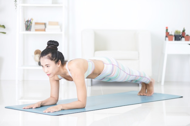 La mujer asiática hermosa de los deportes realiza los ejercicios en casa.