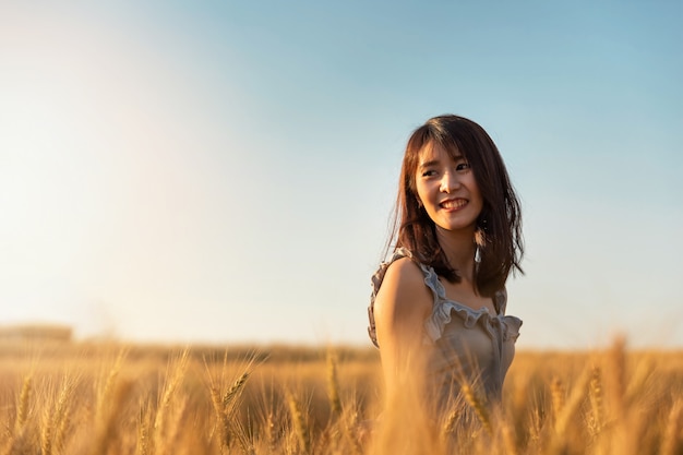 Mujer asiática hermosa y feliz disfrutando de la vida en el campo de cebada al atardecer.