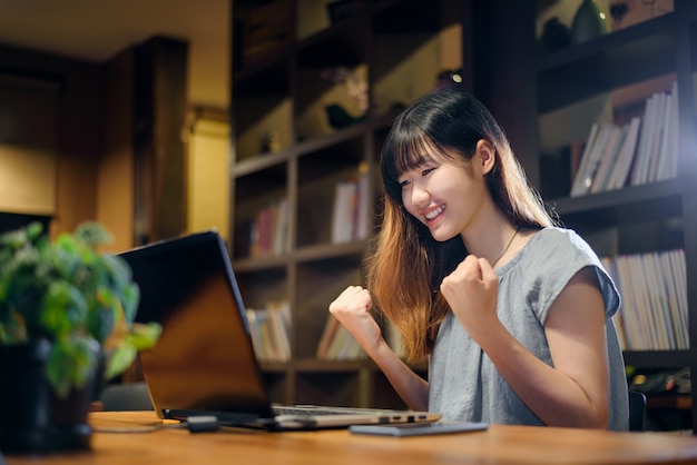 Mujer asiática hermosa feliz del estudiante que trabaja en el ordenador portátil en sitio moderno de la biblioteca