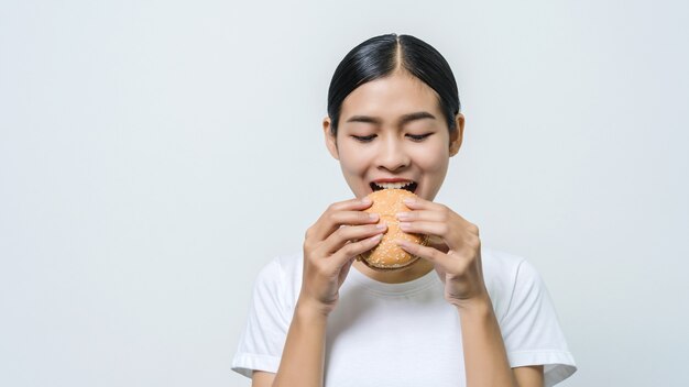 Mujer asiática hermosa joven que come la hamburguesa que se siente feliz.