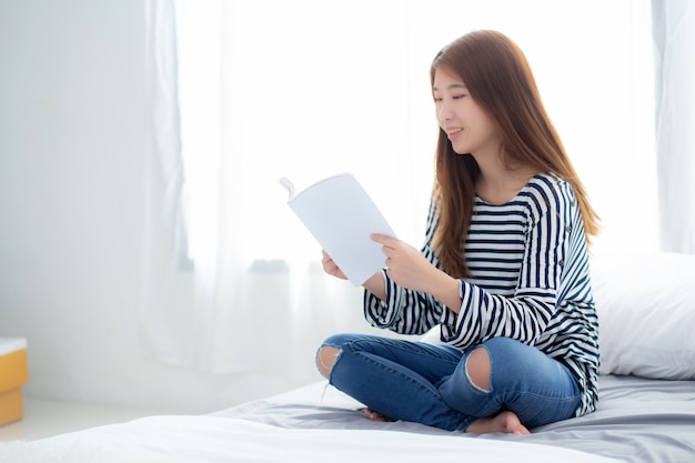 La mujer asiática hermosa relaja el libro de lectura que se sienta en dormitorio