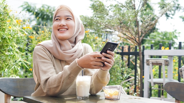 Mujer asiática hijab jugando teléfono en el café