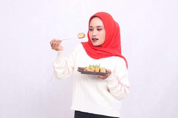 Mujer asiática en hijab sonríe con gracia y franqueza al plato y lleva un plato que contiene sushi