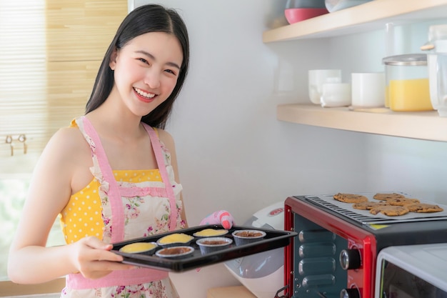 Foto mujer asiática horneando galletas en el horno de su cocina