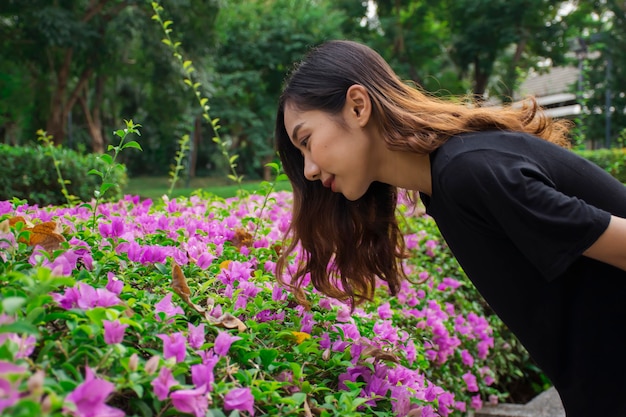 Mujer asiática se inclinó para mirar las flores de color púrpura (buganvillas) con un parque público