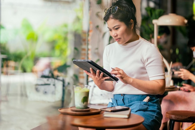 Mujer asiática independiente digital nómada carrera felicidad trabajo alegre sonriente trabajando en línea con dispositivo inteligente tableta teléfono inteligente ocupación en el extranjero proyecto trabajo en cualquier lugar nuevo estilo de vida café