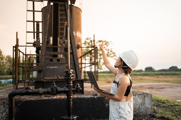 Mujer asiática de ingeniería petroquímica con casco de seguridad de pie en la industria petroquímica de la estructura de la refinería de petróleo