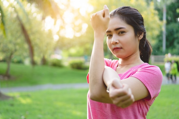 Mujer asiática joven de la aptitud que estira los brazos, el tricep y los hombros antes de ejercicio en parque.