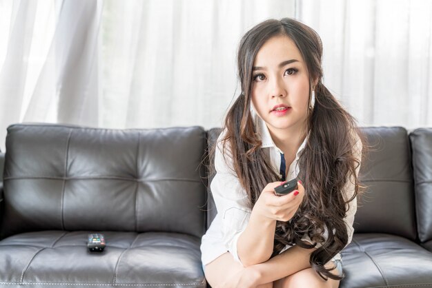 Mujer asiática joven cambiando el canal de televisión en casa en la sala de estar