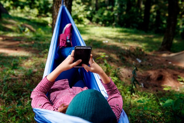 Mujer asiática joven del caminante que usa el teléfono móvil mientras que se relaja en hamaca