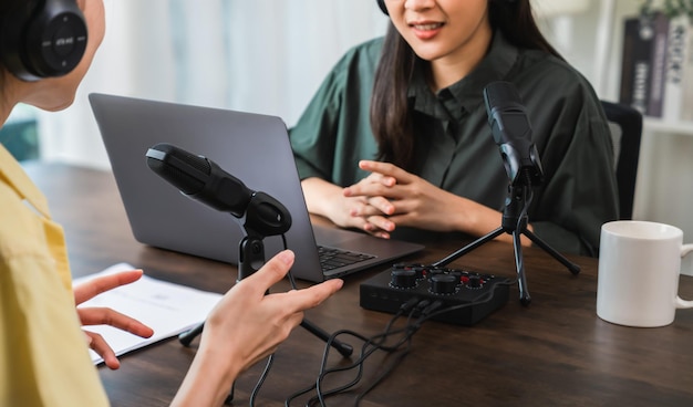 La mujer asiática joven en camisas verdes usa los micrófonos y los auriculares con la entrevista del podcast del registro de la computadora portátil para la radio. Concepto de creador de contenido.