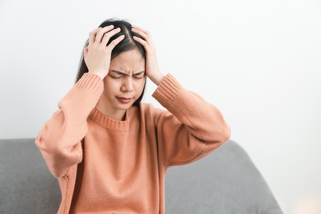 Mujer asiática joven cansada que se sienta y tiene dolor de cabeza debido a la migraña.