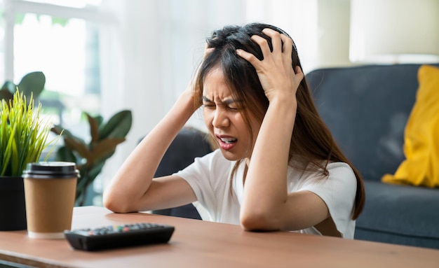 Mujer asiática joven cansada sentada en el sofá y tiene dolor de cabeza porque la migraña