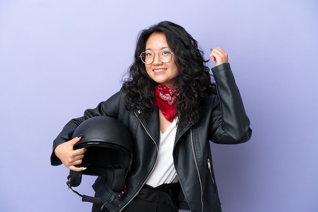 Mujer asiática joven con un casco de motocicleta aislado sobre fondo púrpura celebrando una victoria